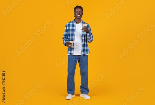 Smiling young black man holding takeaway coffee and smartphone