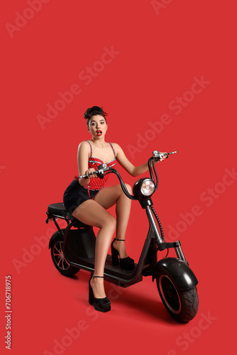 Attractive young pin-up woman riding bike on red background
