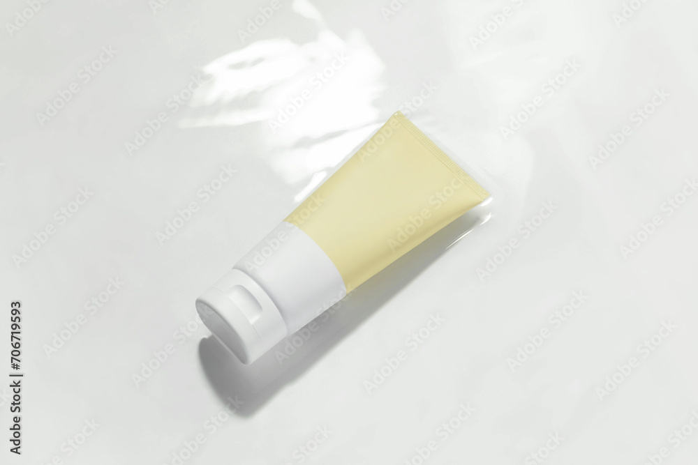 Yellow and white mockup tube of cream in water with reflection on white plain background. Concept of cosmetic beauty products, face and body care. Yellow and white mockup tube of cream in water with reflection on white plain background. Concept of cosmetic beauty products, face and body care.
