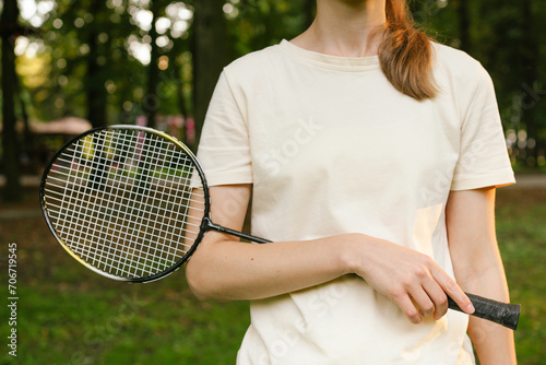 Close-up of a young woman in a t-shirt holding a badminton racket in her hand. Concept of outdoor sports games, competition and pastime © Daryna 