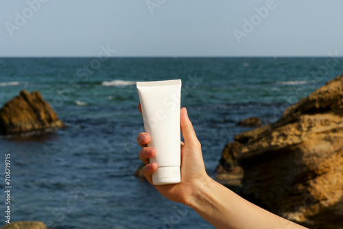 Female hand holding a white tube of cream mockup on the background of sea water and sky. The concept of natural products of beauty and aesthetics © Daryna 