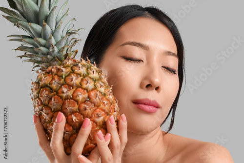 Pretty young Asian woman with pineapple on grey background