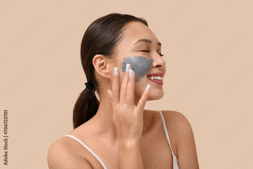 Young woman with clay mask on her face against beige background Young woman with clay mask on her face against beige background