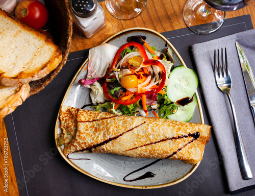 Appetizing savory stuffed thin pancake with vegetable salad of greens, cucumber, bell pepper and yellow cherry tomatoes. photo