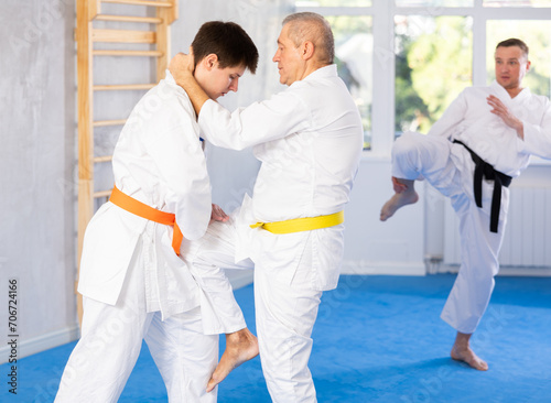 Young man and elderly man in kimonos train judo techniques in studio