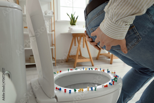 Young man with hemorrhoids and paper pins on toilet bowl in restroom, closeup