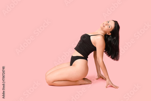 Body positive young woman in underwear sitting on pink background