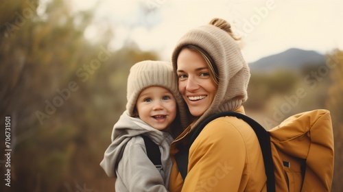 Mom and her cute little son, woman carrying the male child or kid on her back, both of them are smiling and looking at the camera. Walking outdoors in cold weather, motherhood concept, little boy