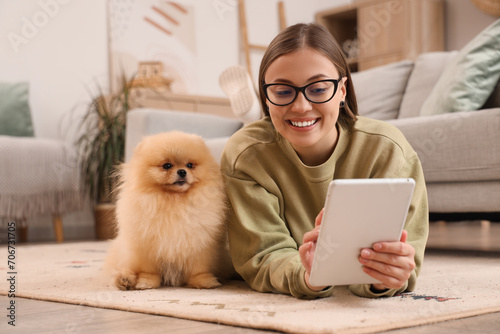 Young woman with cute Pomeranian dog using tablet computer on floor at home photo
