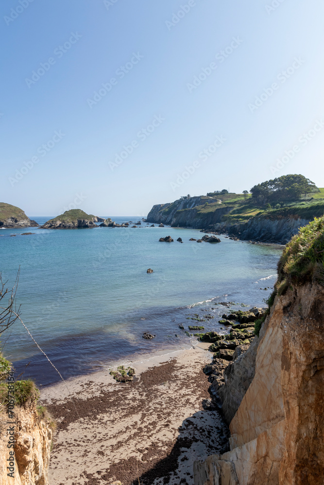 coastal landscape with clear blue waters, rocky shores, lush greenery, and a bright, cloudless sky