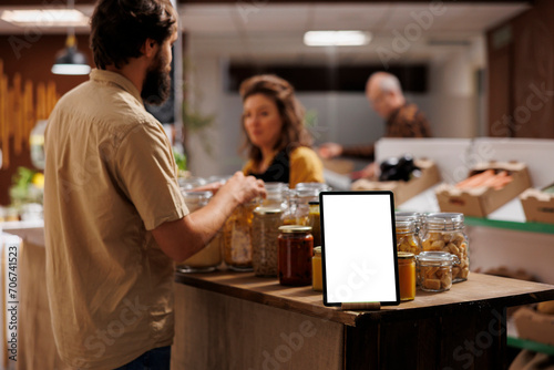 Mockup tablet with empty copy space used as advertising sign in zero waste supermarket with customers shopping for healthy food in blurry background. Isolated screen device in grocery shop