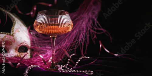 Masquerade ball holiday background. Glass of rose champagne, Venetian carnival mask and feathers on dark burgundy velour background