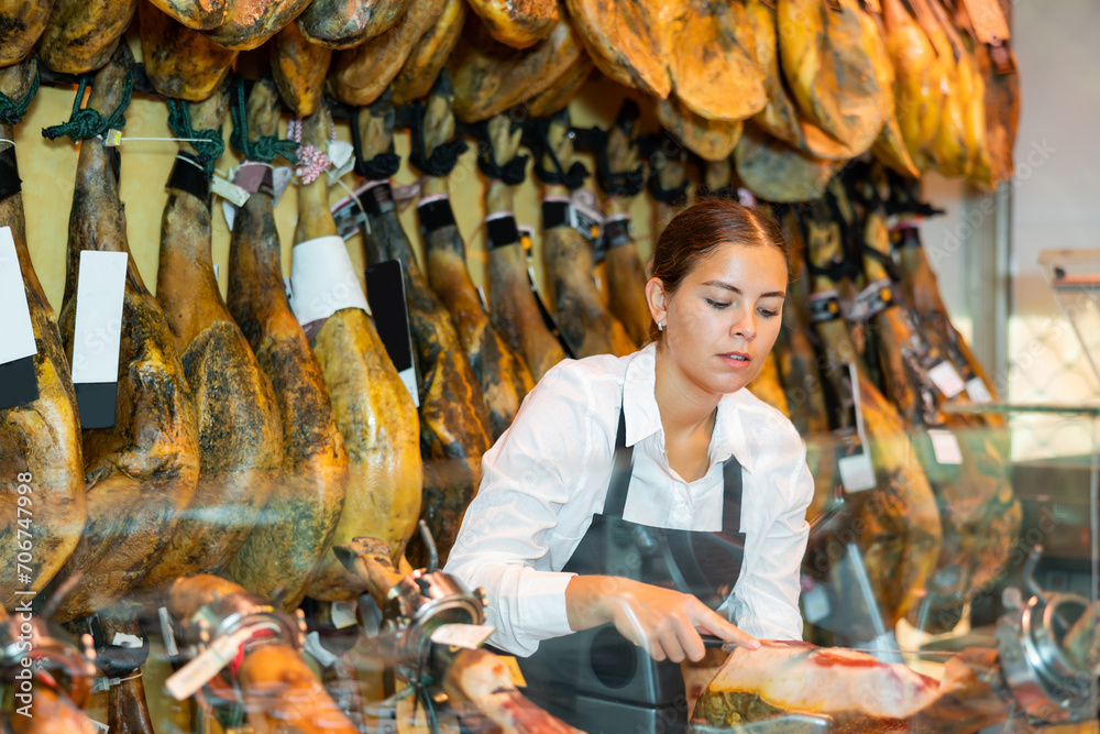 Young female seller of butcher store preparing jamon of lamb for sale