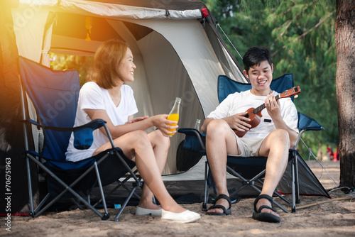 An outdoor serenade, A beaming Asian couple, by their tent, shares a song on the ukulele, capturing the essence of togetherness and happiness. Music and love unite at the campsite. Camping putdoor photo