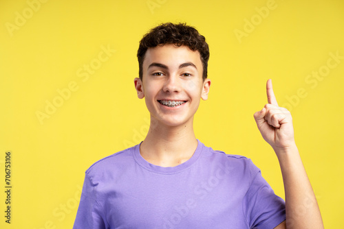 Smiling excited boy wearing casual purple t shirt looking at camera showing finger on copy space