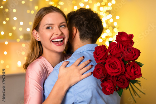Radiant woman hugging man with bouquet of roses, gleeful surprise