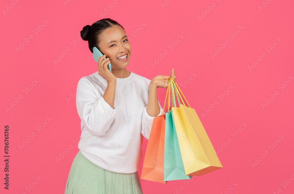 Portrait of smiling asian woman talking on cellphone and holding shopping bags