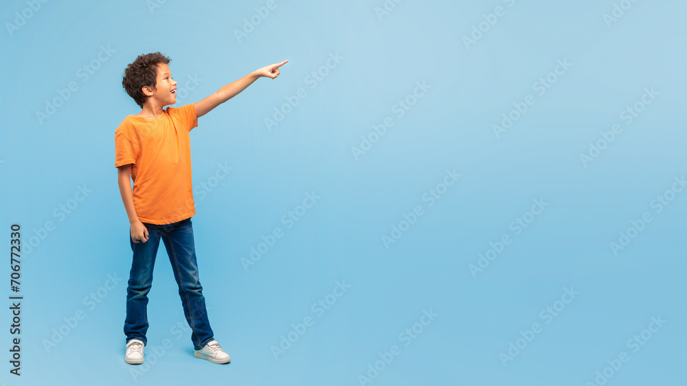 Excited boy pointing in the air at free space on blue backdrop Excited boy pointing in the air at free space on blue backdrop