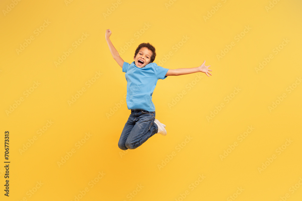 Ecstatic black boy jumping with joy on yellow background