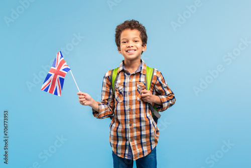Smiling child boy with UK flag, backpack, blue background