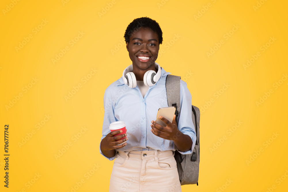 A black woman student multitasking with a coffee in one hand and a phone in the other A black woman student multitasking with a coffee in one hand and a phone in the other