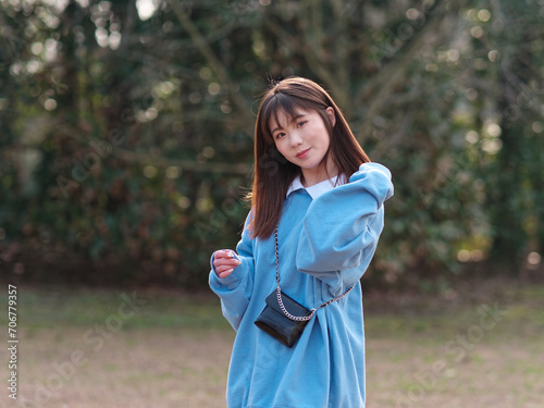 Beautiful young Chinese woman posing in sunny summer forest, wearing blue loose oversized top and miniskirt with small shoulder bag. Emotions, people, beauty, youth and lifestyle portrait. © atiger