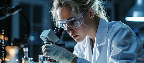 My analysis Content promising blond scientist holding blood test tubes and wearing a uniform and medical gloves while sitting near a microscope. with copy space image. Place for adding text or design photo