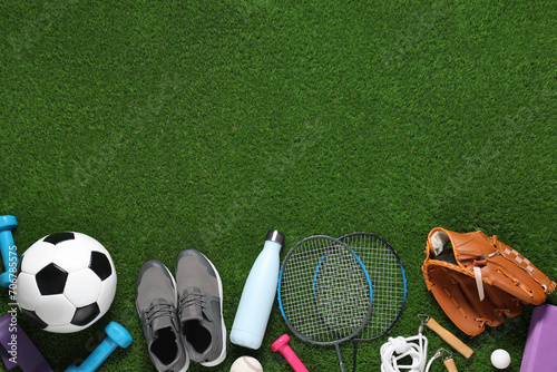 Different sports equipment on green grass, flat lay. Space for text