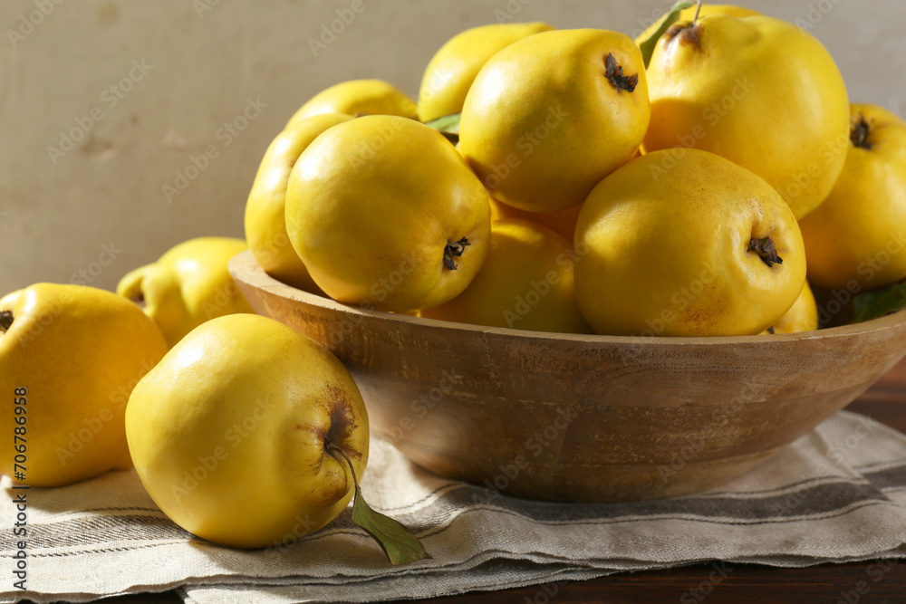 Tasty ripe quince fruits in bowl on wooden table, closeup