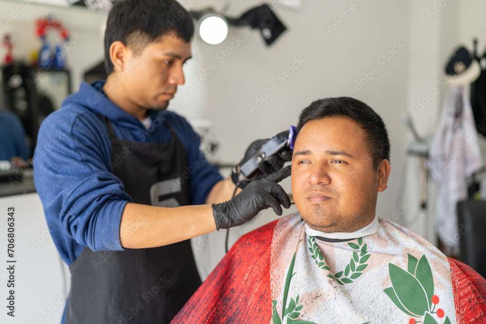 Latin young barber attending a client in a barber shop Latin young barber attending a client in a barber shop