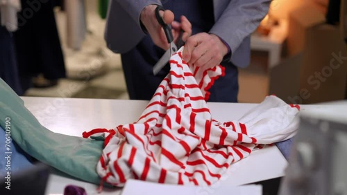Close-up. An irritated man cuts white clothes with red stripes with scissors and nervously throws them on the table photo