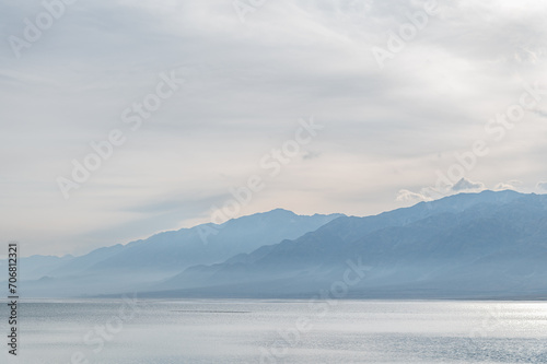 Bluish silhouettes of misty mountains and lake.  Orto-Tokoy reservoir in Kyrgyzstan in winter.