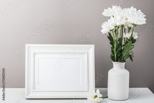Empty photo frame and a bouquet of white chrysanthemums, daisies in a white vase on a gray background. Postcard, congratulation, home interior.