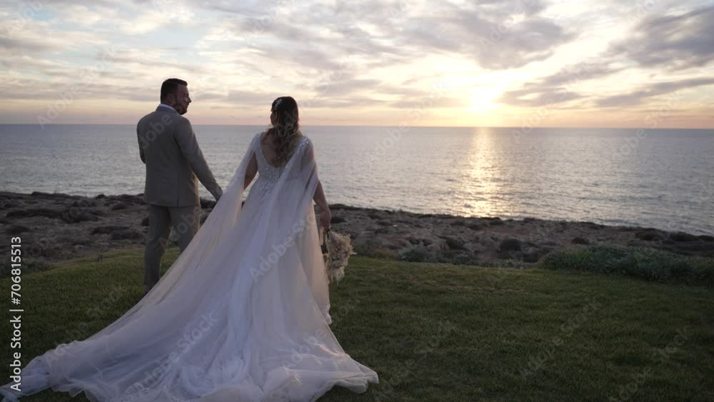 Cinematic rotating shot around a bride and groom standing on the coast looking out over the water at sunset. Cinematic rotating shot around a bride and groom standing on the coast looking out over the water at sunset.