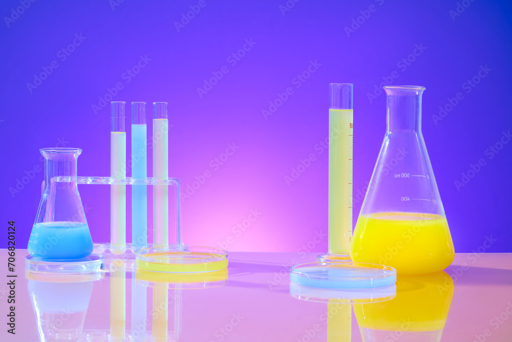 Test tubes, Erlenmeyer flasks, and petri dishes hold yellow and blue solutions on a pink-purple gradient background. Dedicated space for product preparation. Test tubes, Erlenmeyer flasks, and petri dishes hold yellow and blue solutions on a pink-purple gradient background. Dedicated space for product preparation.