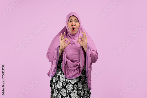 Fat Asian Muslim women make an OK hand gesture with happy facial expressions. Wearing pink hijab. isolated on a pink background