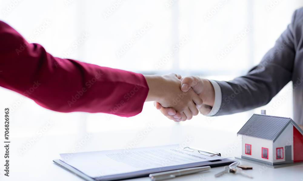 Real estate agent shakes hands with a client to sign a home purchase contract congratulating the client on the purchase. Real estate agent shakes hands with a client to sign a home purchase contract congratulating the client on the purchase.