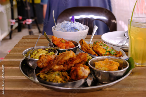 A bowl of Blue Butterfly Pea Flower coconut rice served with a few popular local dishes like chicken curry and sweet and sour fish in a local restaurant. A mix of Indian, Malay, and Peranakan food