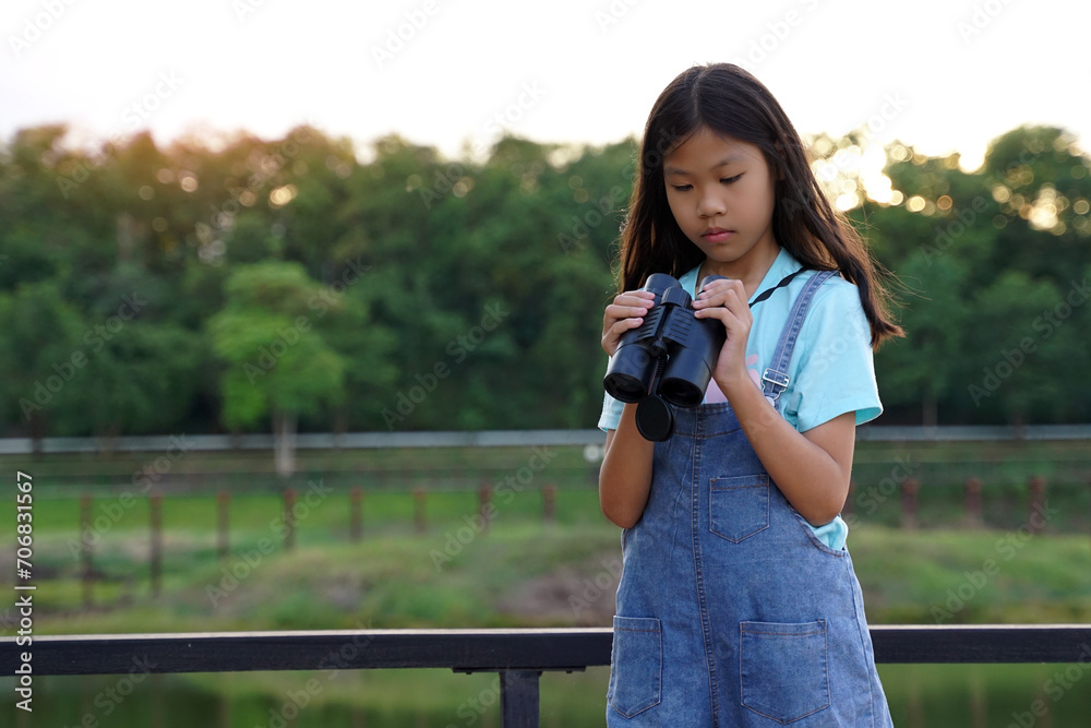 Asian girl uses binoculars to observe the nature, birds, and animals of the National Park while camping with her family. with the concept of learning outside the classroom nature study, exploration.  