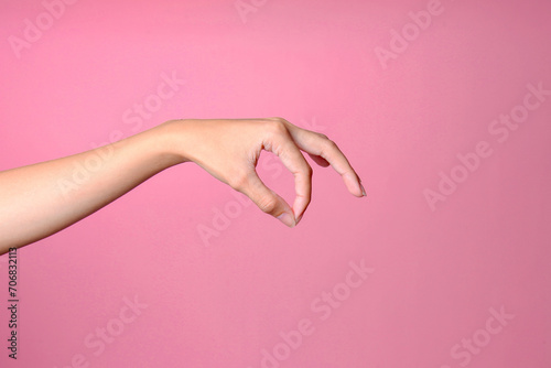 Woman hand holding or picking something up, isolated on pink background