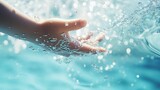 Hand is playfully catching sparkling water droplets against a blurred blue background illuminated by daylight. Pool.