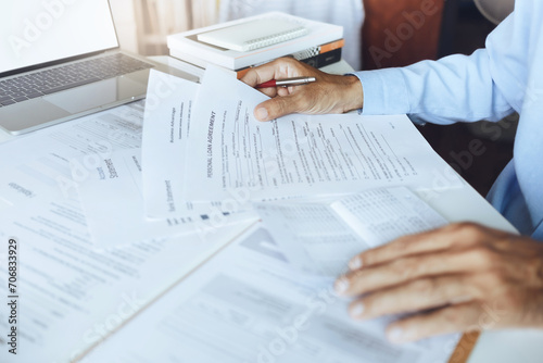 Hand of businessman holding personal loan agreement documents checking contract details and amount in the passbook to apply for a loan to start a new business photo