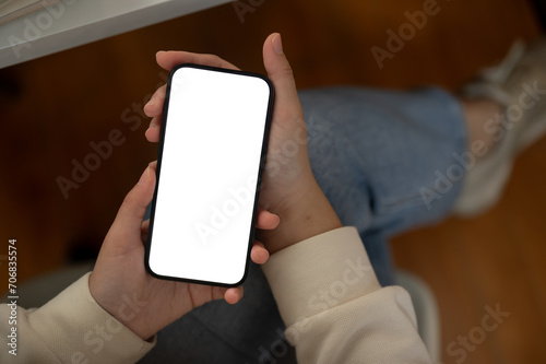 Top view of a woman is using her smartphone while sitting indoors. A white-screen smartphone mockup