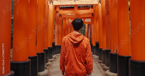 Man, outdoor and walk by shinto torii gate, back and culture for thinking, ideas and nature in forest. Person, statue and memory on spiritual journey, Fushimi Inari shrine and architecture in Kyoto photo