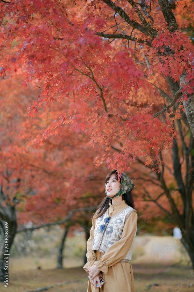Asian woman in casual dress enjoys Japan's beauty, walking amid vibrant foliage. A cheerful holiday portrait capturing the essence of nature, fashion, and a journey.