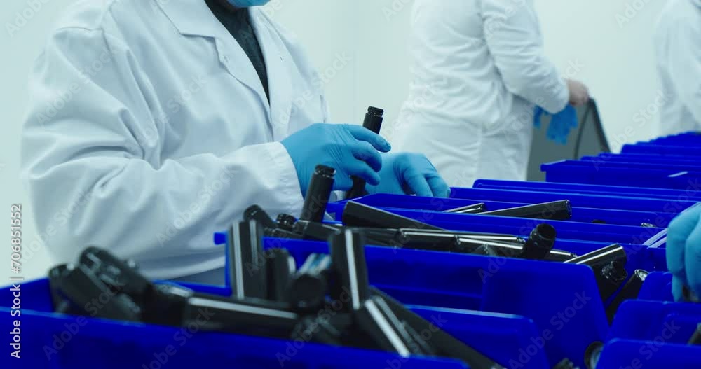 Lab technician on the assembly line packs cannabis pre-rolls into a tube that will be sold in dispensaries. Technician in the background puts on gloves. Medium shot. SLOW MOTION Lab technician on the assembly line packs cannabis pre-rolls into a tube that will be sold in dispensaries. Technician in the background puts on gloves. Medium shot. SLOW MOTION