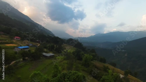 Aerial FPV drone swoops along lush cliff in Pokhara Nepal to reveal red roof school buildings photo