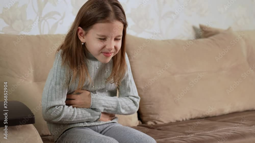 Girl with abdominal pain sitting on a sofa and holds her stomach Girl with abdominal pain sitting on a sofa and holds her stomach