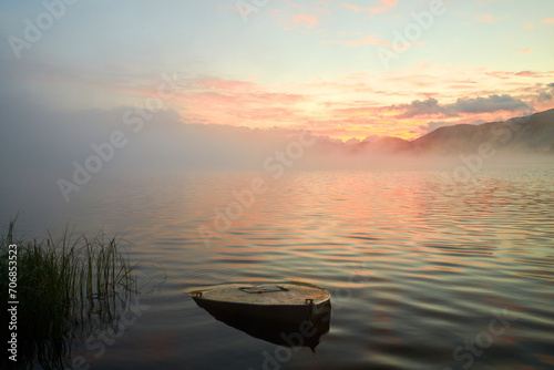 Atmospheric morning fog over Lake Yazevoe in eastern Kazakhstan. Lake Yazevoe is located at an altitude of 1685 meters above sea level. A sunken boat in the foreground.  Blur effect.    © Yerbolat