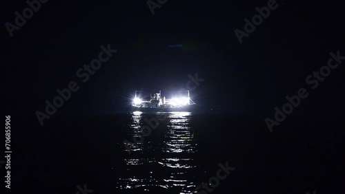 밝은 불을 킨 오징어잡이 배가 어두은 밤 바다에 홀로 떠있다 photo